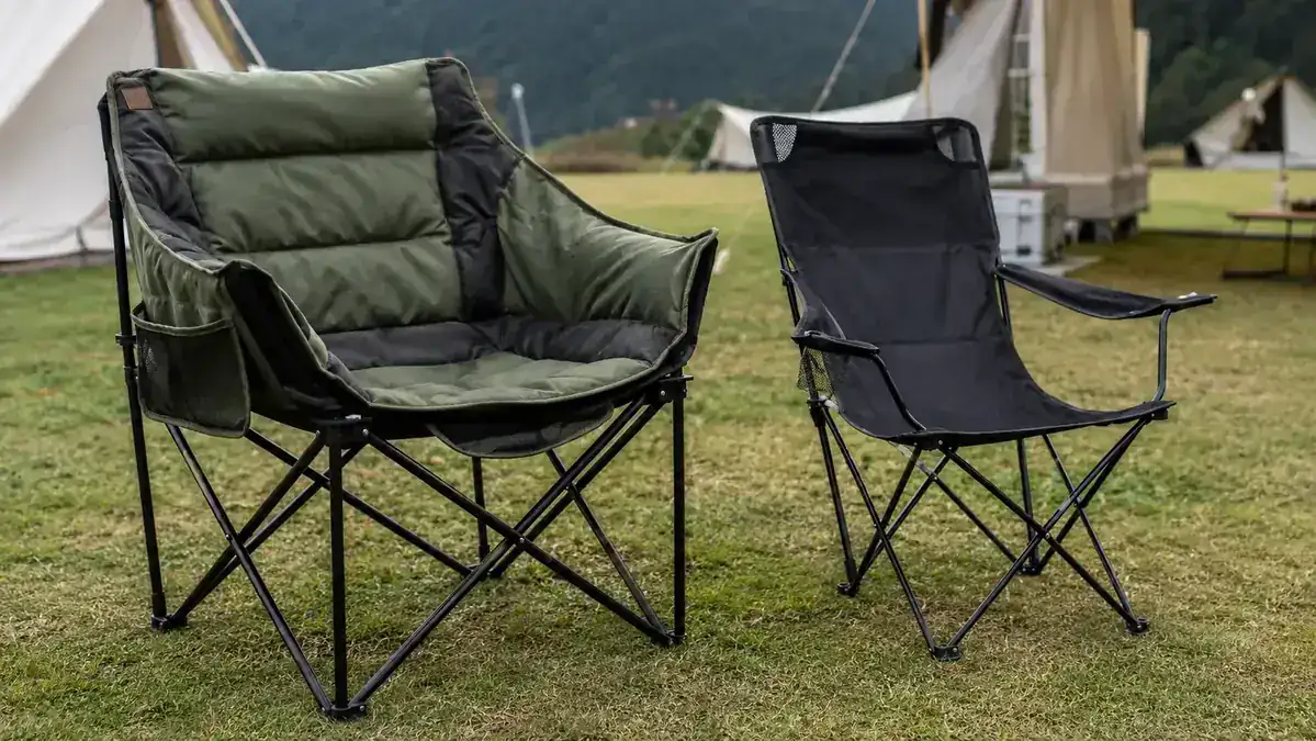 Wide padded camping chair next to a narrow basic folding chair on grass, side-by-side size comparison