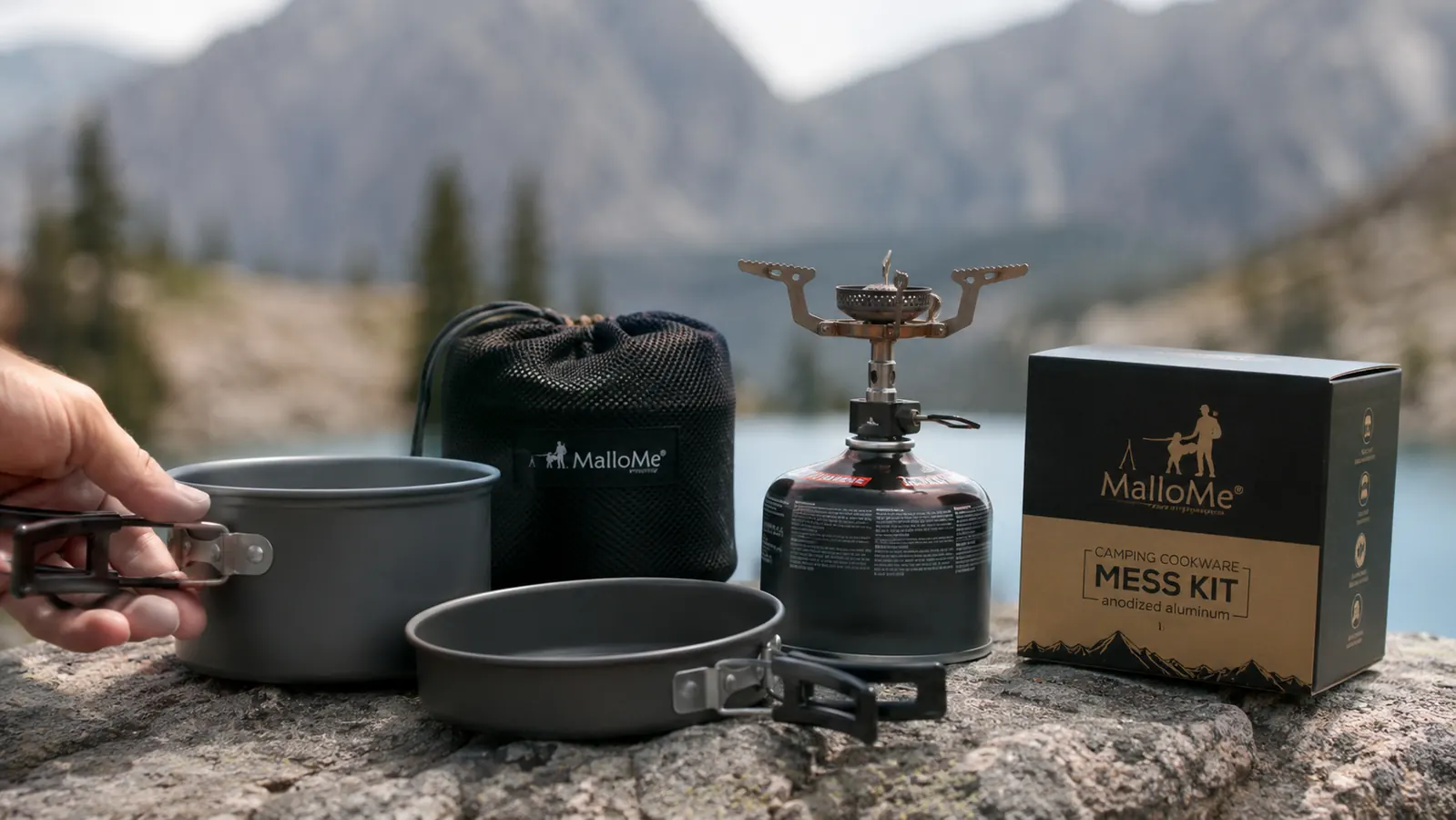 MalloMe camping mess kit with pot, pan, and utensils arranged on a flat rock near a camp stove